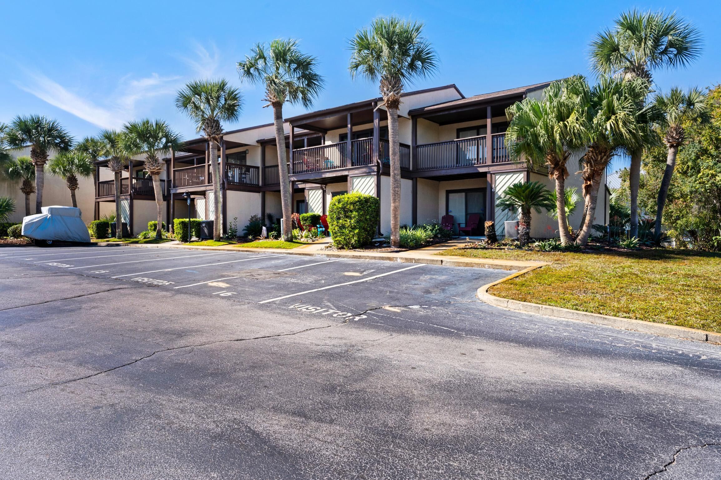 A multi-story hotel with balconies, palm trees, and a parking lot.