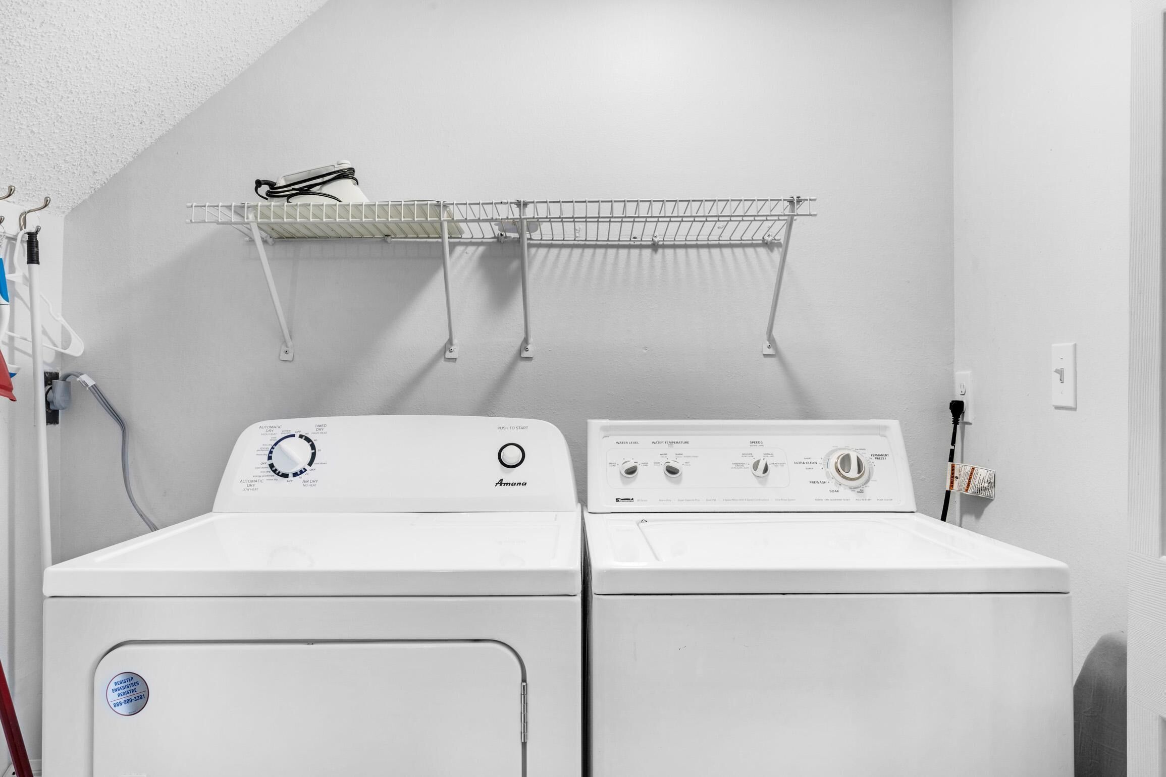 A laundry area with two white front-loading washing machines and a metal drying rack above them.