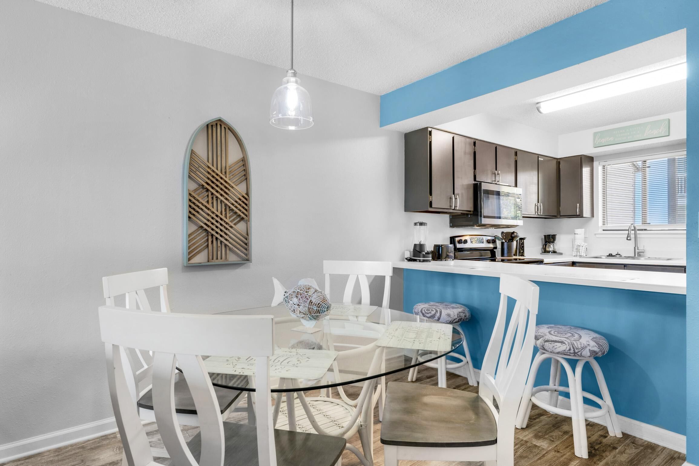 A modern kitchen with white cabinets, a blue accent wall, and a dining area with white chairs and a glass table.