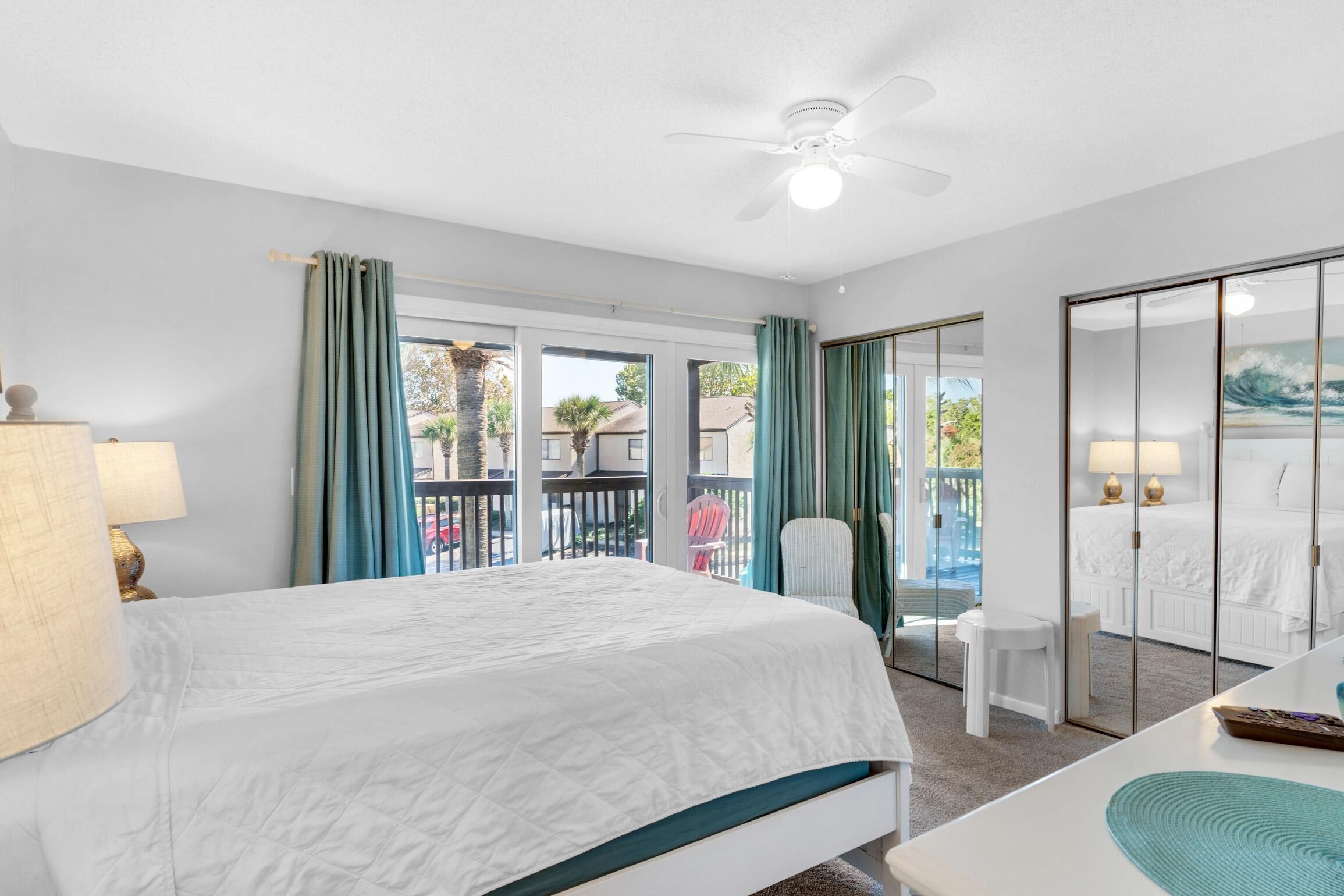 A hotel room with a bed, a desk, a chair, a balcony with a view, and a ceiling fan.