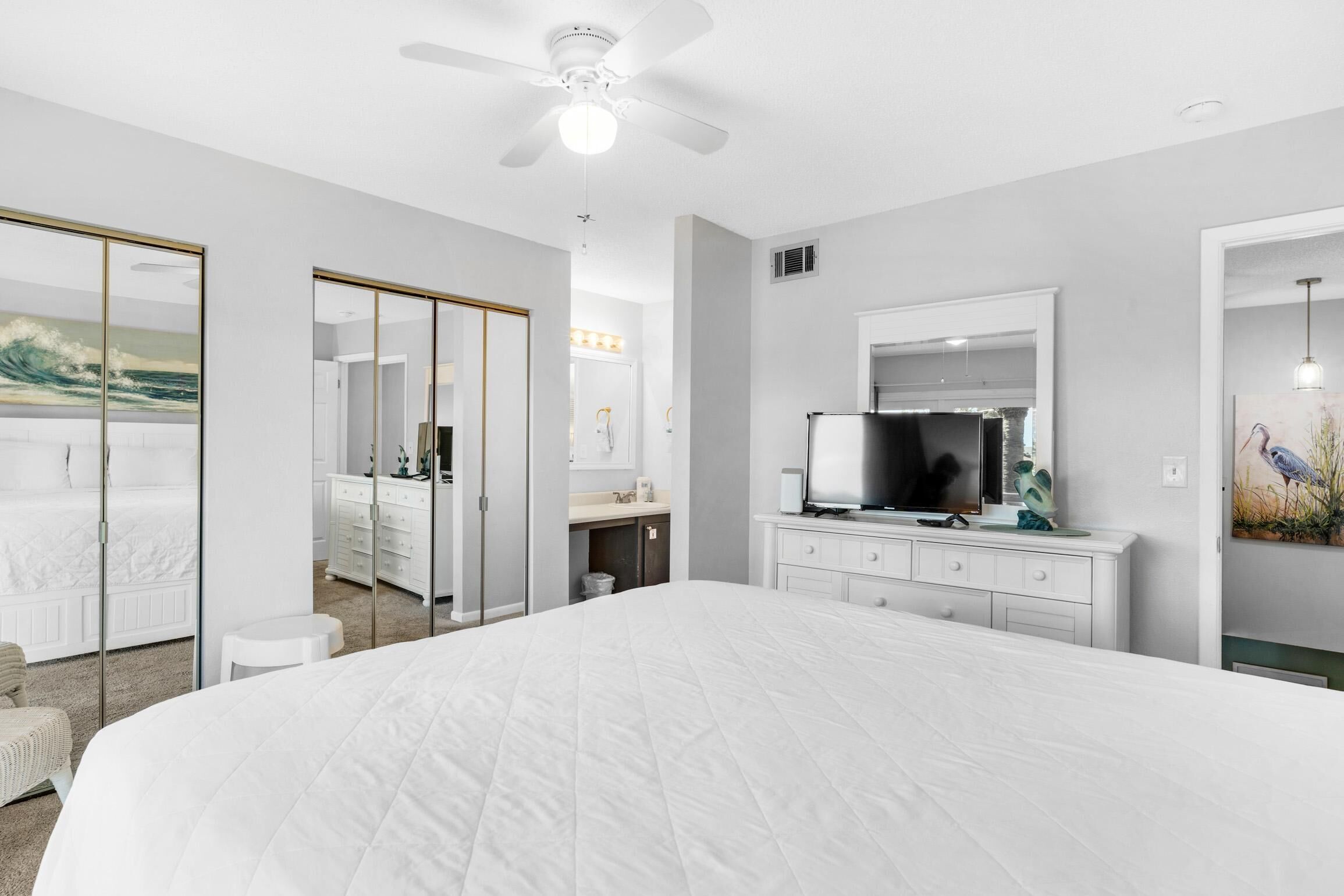 Un dormitorio moderno con una cama grande, un ventilador de techo, un televisor y un espejo.