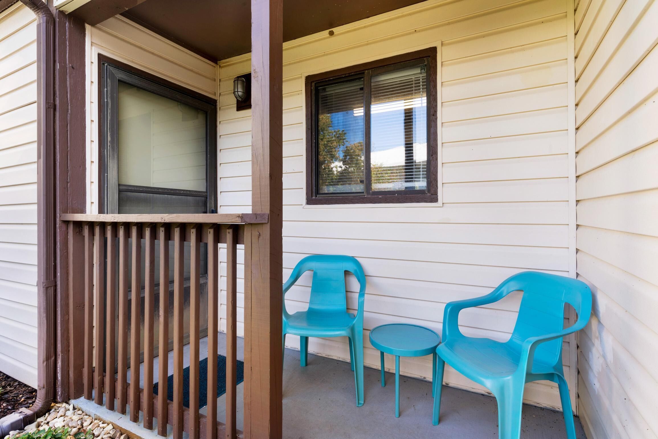A porch with a wooden railing, two turquoise plastic chairs, and a small round table.