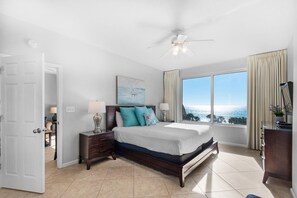 A bedroom with a large bed, a nightstand, a dresser, and a window with a view.