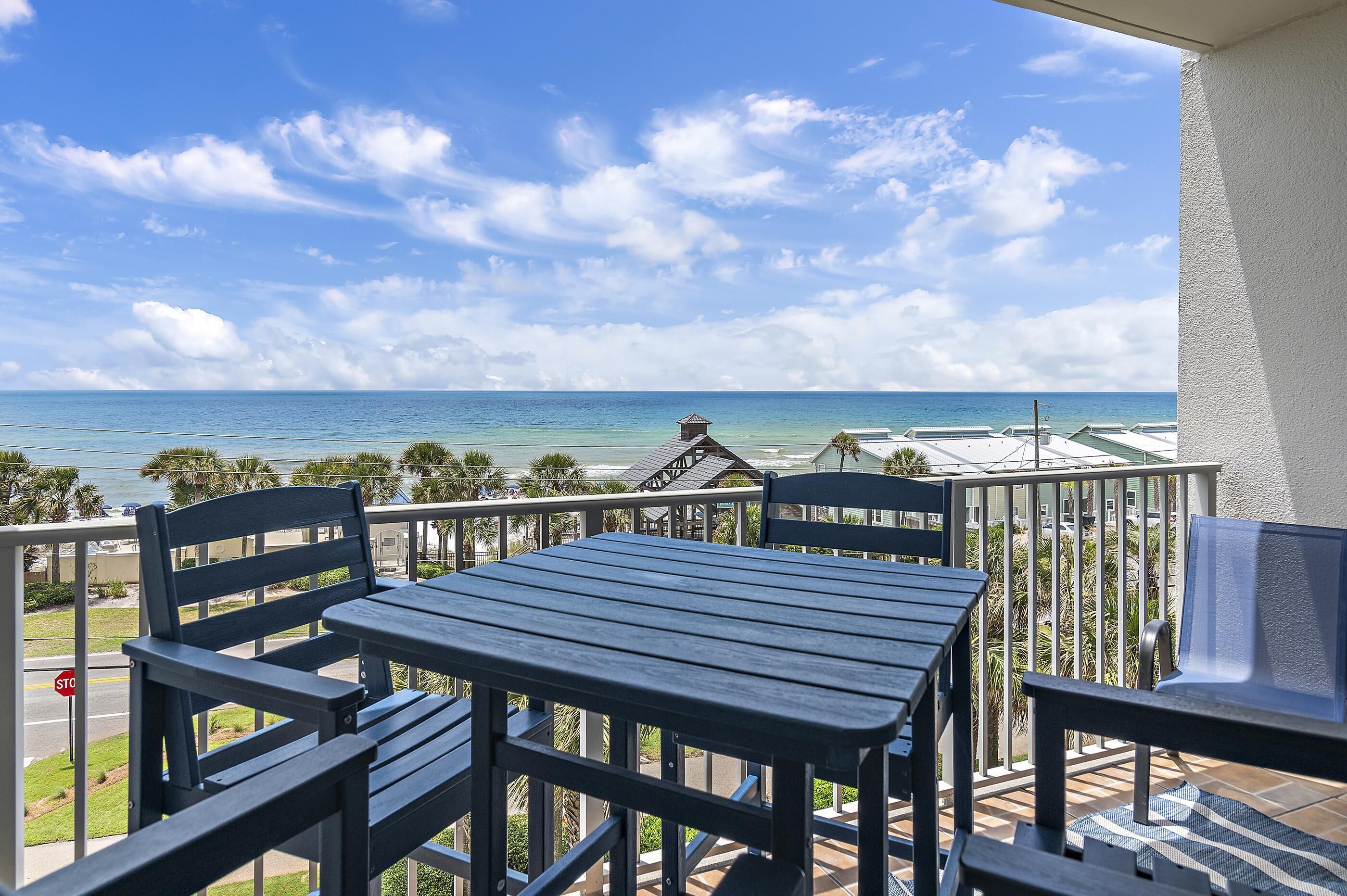 A balcony with a table and chairs overlooking a beach.