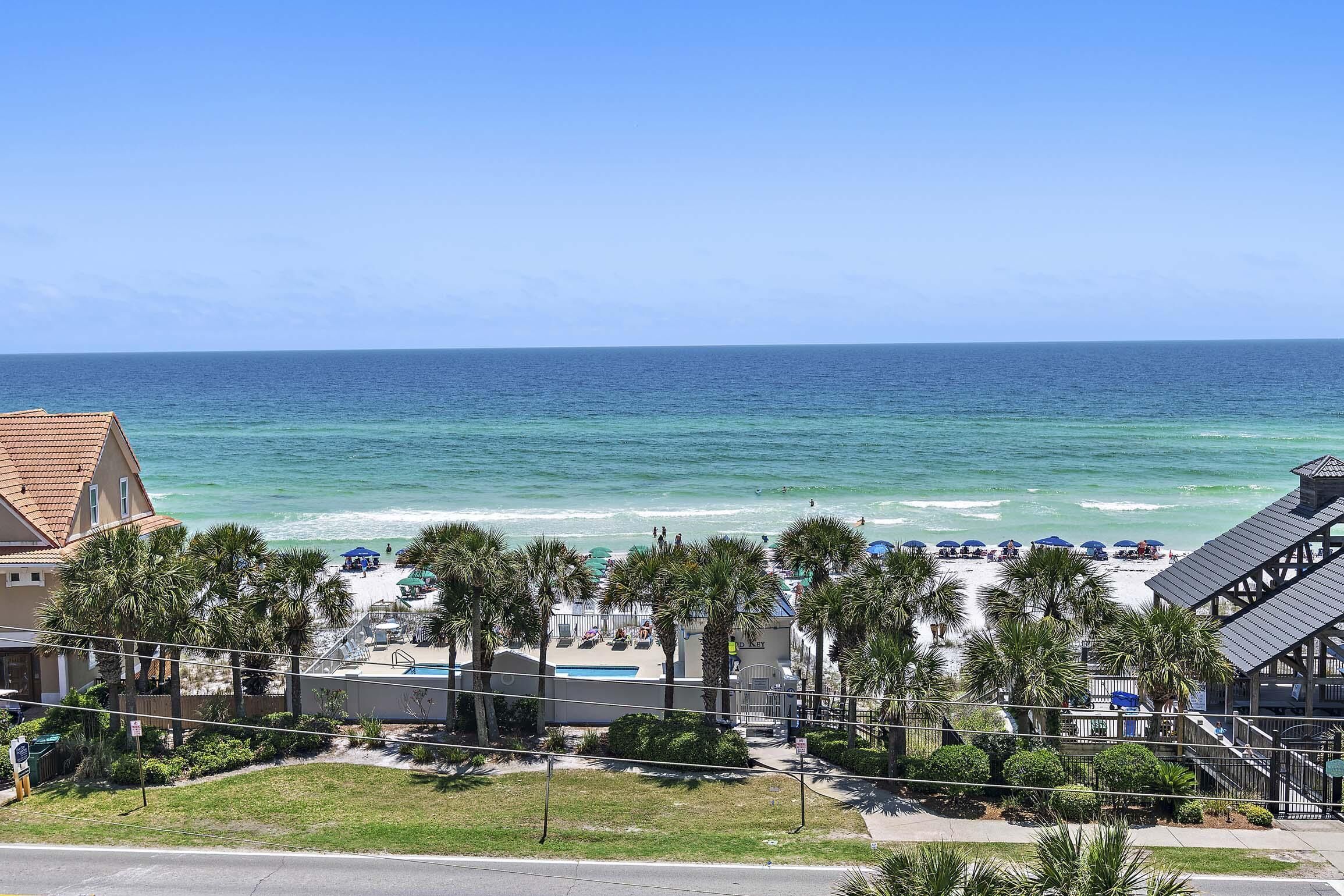 A beachfront hotel with a pool, palm trees, and beach umbrellas.