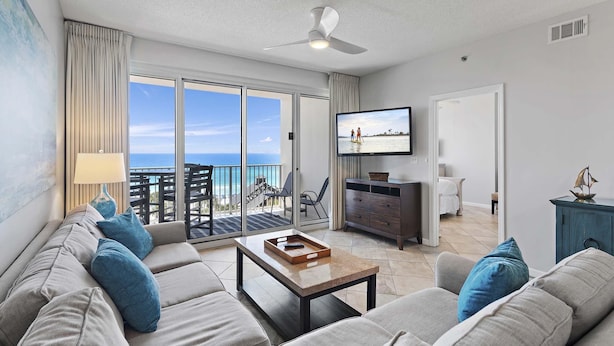 Ein modernes Wohnzimmer mit einer Couch, einem Couchtisch und einem Fernseher. Es gibt einen Balkon mit Blick auf den Ozean.