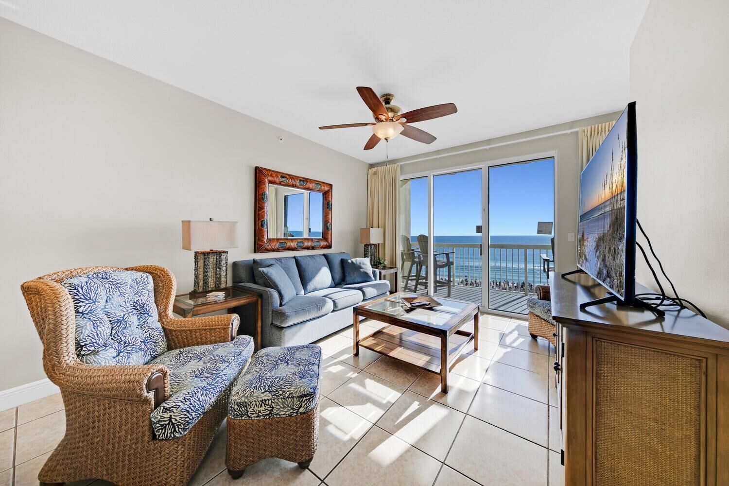 Een ruime woonkamer met een bank, twee fauteuils, een salontafel, een televisie, en een balkon met uitzicht op de oceaan.