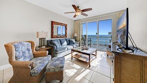 Un salon spacieux comprenant un canapé, deux fauteuils, une table basse, un téléviseur et un balcon avec vue sur l’océan.