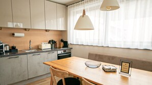 A modern kitchen with a wooden table, two chairs, a sink, and a window with sheer curtains. - Lovely home in Rennweg am Katschberg (Rennweg am Katschberg)