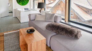 A modern living room with a grey sofa, a wooden coffee table, and a view of wooden buildings through large windows. - Lovely home in Rennweg am Katschberg (Rennweg am Katschberg)