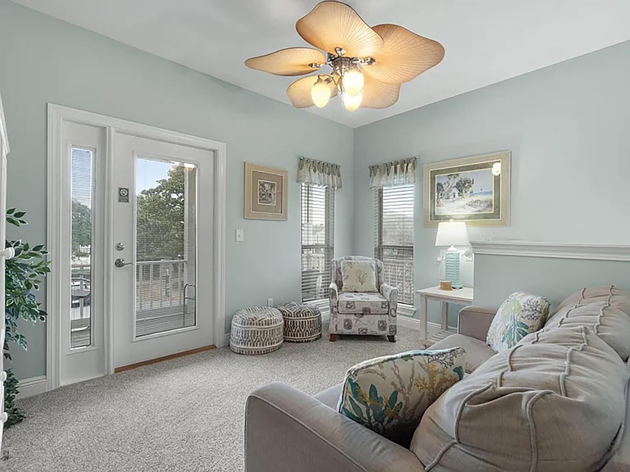 A living room with a beige sofa, a patterned armchair, a ceiling fan, and a door leading to a balcony.