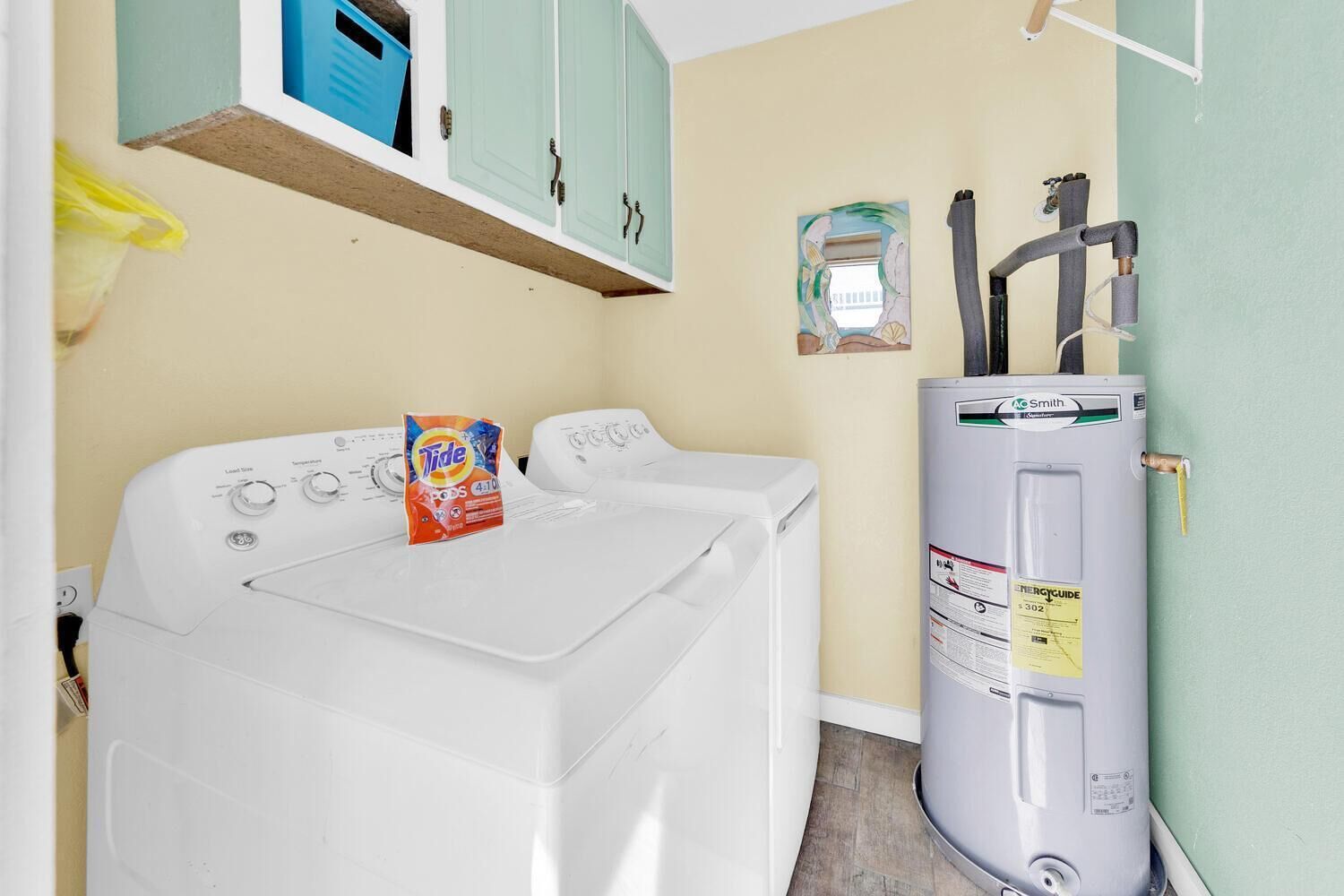 A laundry room with a front-loading washer and dryer, a water heater, and a shelf above the washer.