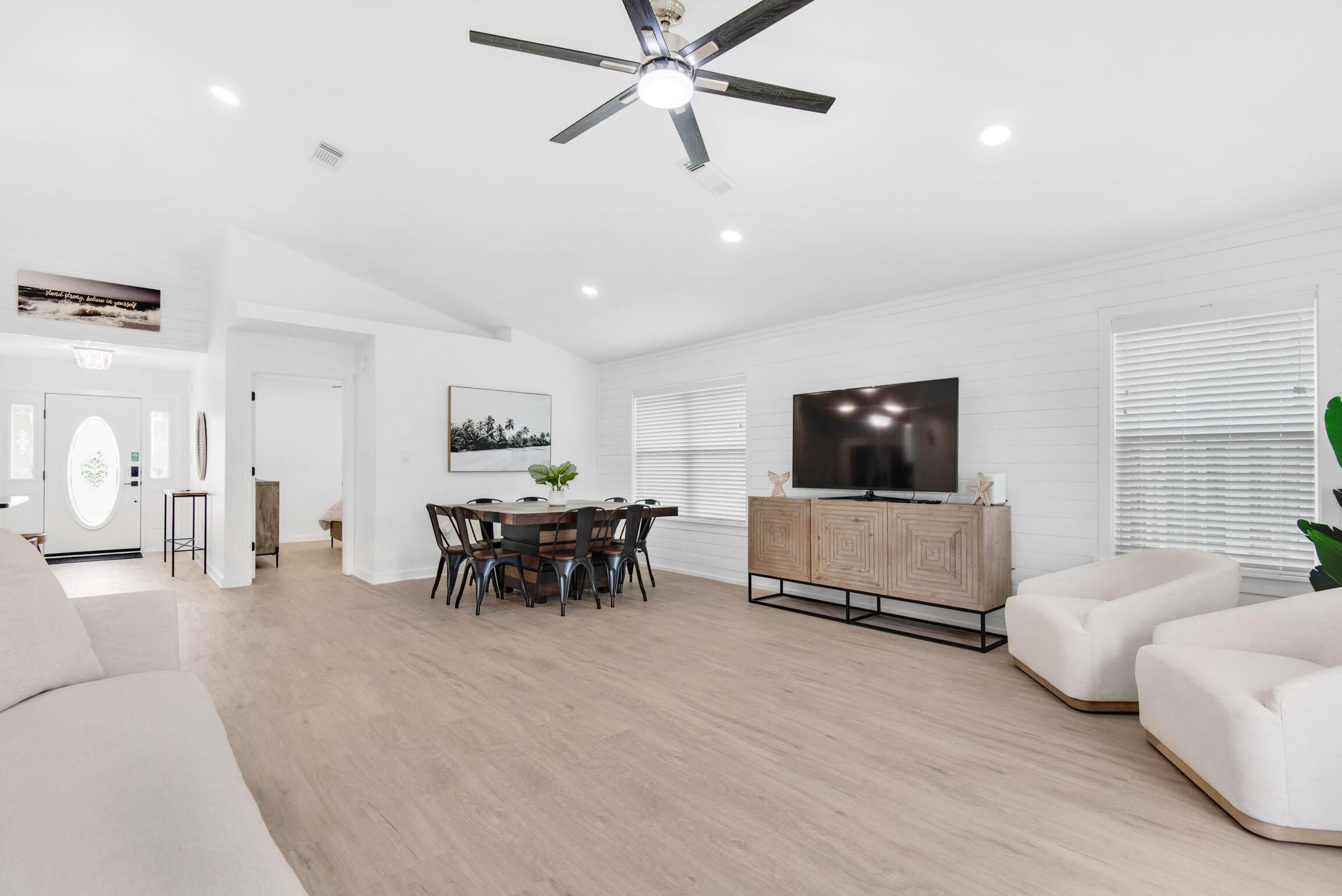 A modern living room with a dining area, a flat-screen TV, and a ceiling fan.