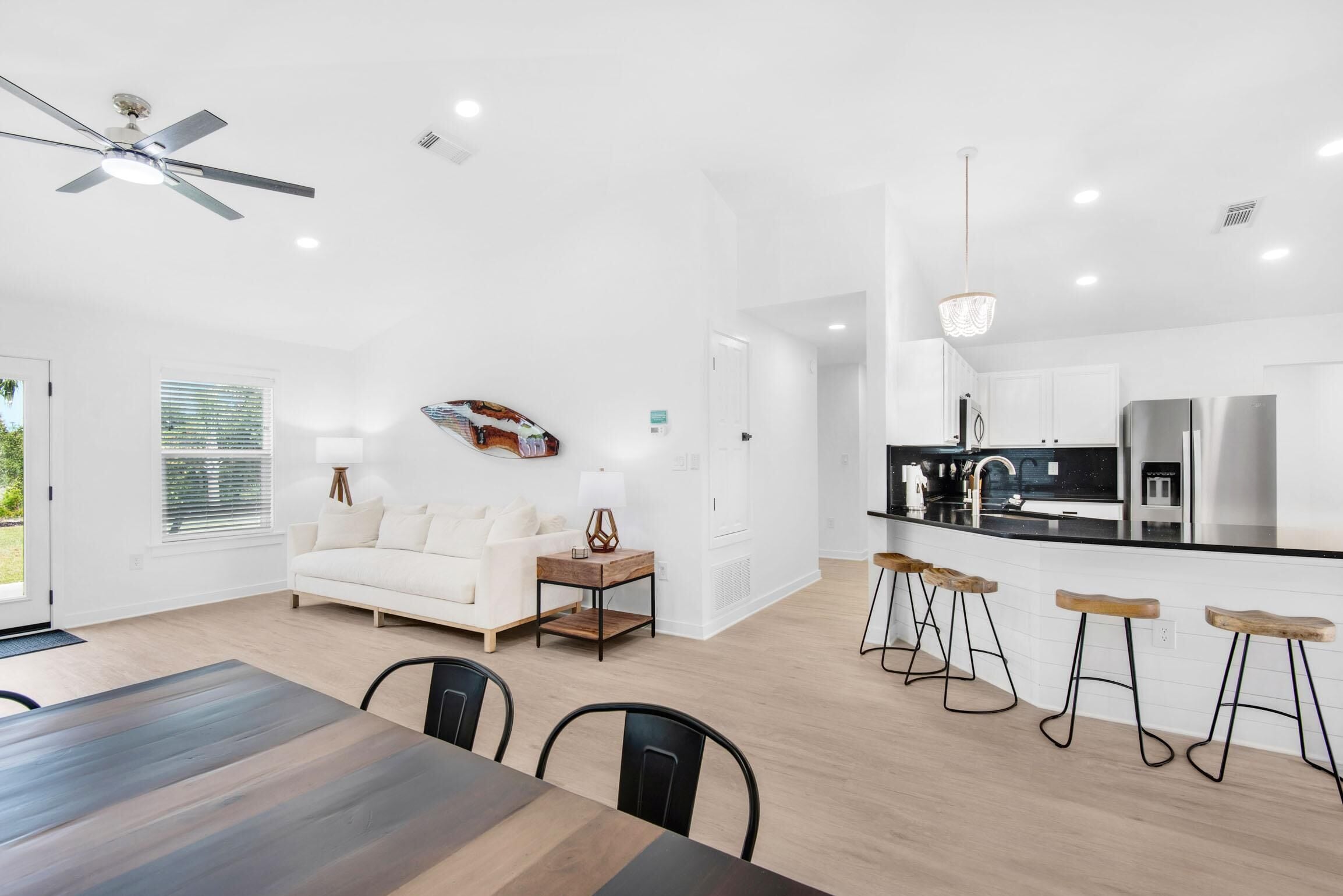 A modern kitchen with a black countertop, stainless steel appliances, and wooden stools.