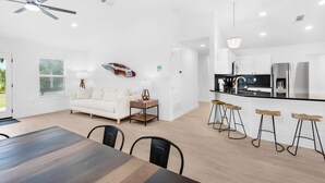 A modern kitchen with a black countertop, stainless steel appliances, and wooden stools. - Destin4relaxin (Miramar Beach)