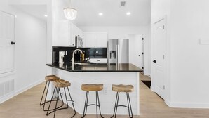 A modern kitchen with white cabinetry, a black countertop, and three wooden stools. - Destin4relaxin (Miramar Beach)