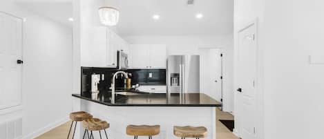 A modern kitchen with white cabinetry, a black countertop, and three wooden stools.