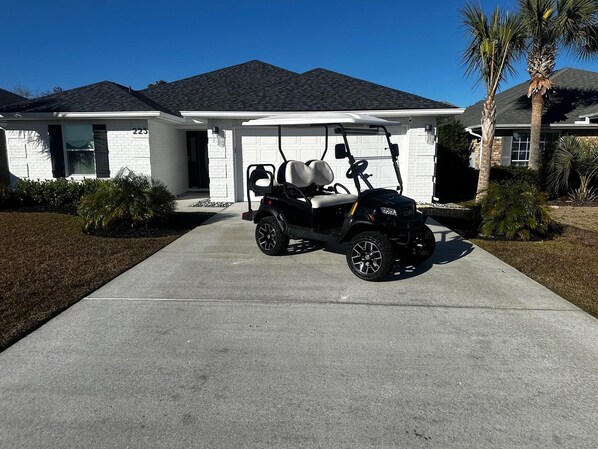 A house with a garage, a golf cart parked in the driveway, and palm trees in the yard.