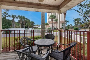 A covered outdoor seating area with a table and chairs, overlooking a street with palm trees and a white picket fence. - Aloha Cottage (Miramar Beach)