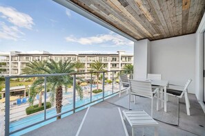 A balcony with a view of a swimming pool and palm trees, white furniture, and a wooden ceiling. - The Pointe 1-134 (Panama City Beach)