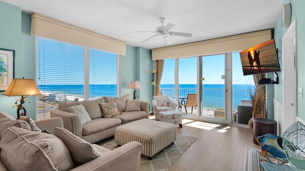 A spacious living room with a large window overlooking the ocean, a ceiling fan, and a flat-screen TV mounted on the wall. - Leeward Key 806 (Miramar Beach)