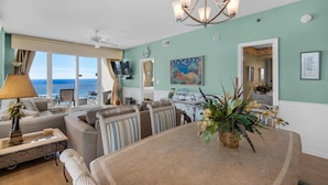 A spacious living room with a large dining table, comfortable seating, a chandelier, and a view of the ocean. - Leeward Key 806 (Miramar Beach)