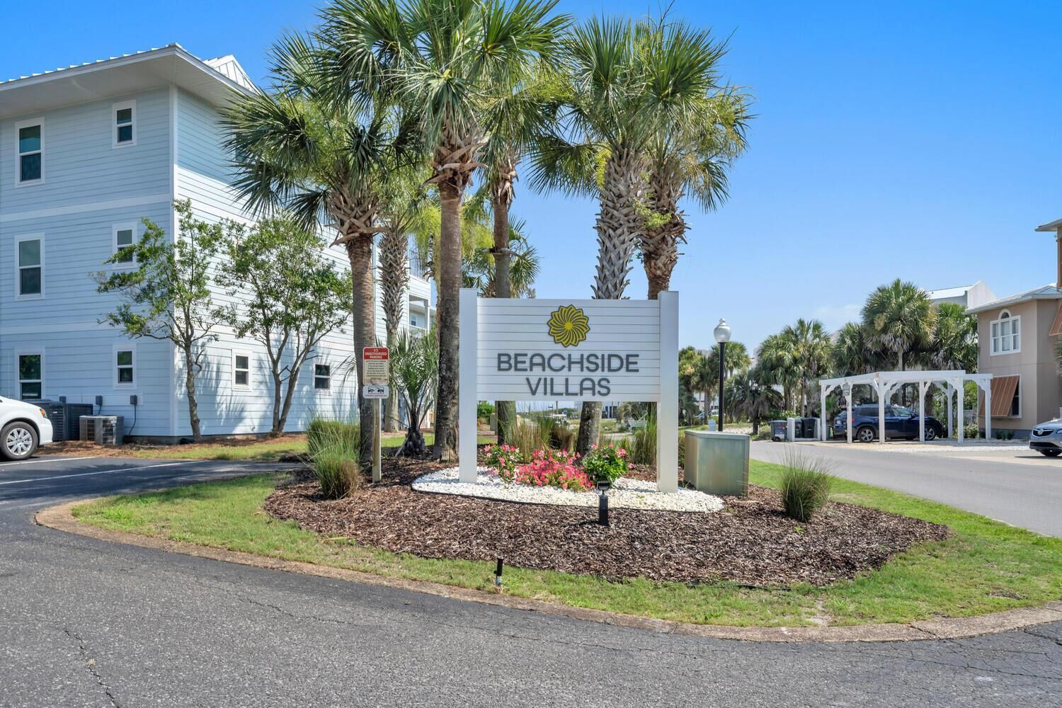 A sign for 'Berchside Villas' with a clear view of the surrounding area including palm trees and a white building.
