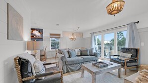 A spacious living room with a grey sofa, wooden chairs, a coffee table, and a balcony with a view. - Beachside Villas 1123- A Sandy Carol (Santa Rosa Beach)