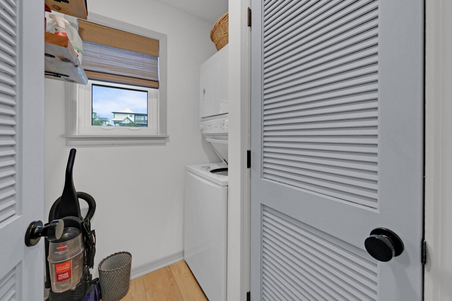 Un cuarto de lavandería con lavadora, secadora y ventana con vista a una casa.