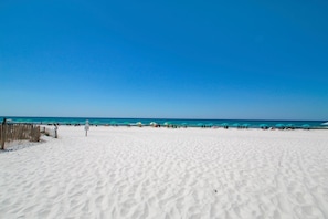 Ampia spiaggia sabbiosa con una recinzione in legno a sinistra e diversi ombrelloni in lontananza.