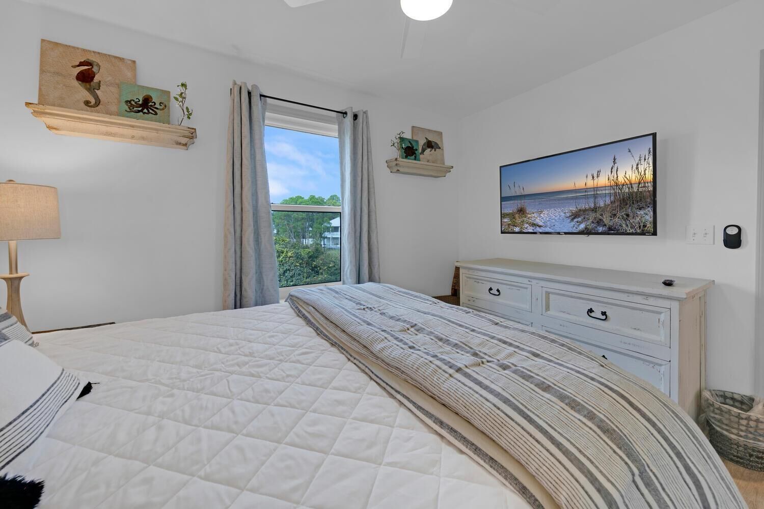 Quarto com cama, penteadeira, televisão e obras de arte nas paredes.