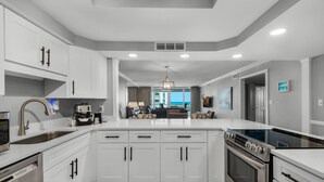 A modern kitchen with white cabinetry, a built-in oven, and a large island with a sink. - Shoreline Towers 2023 (Destin)