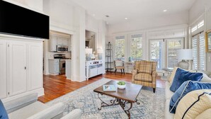 A spacious living room with a large coffee table, a sofa, and a chair. There is a kitchen area with white cabinets and a microwave. - Ebb Tide, Steps from the Beach & Community Pool (Saint Simons Island)