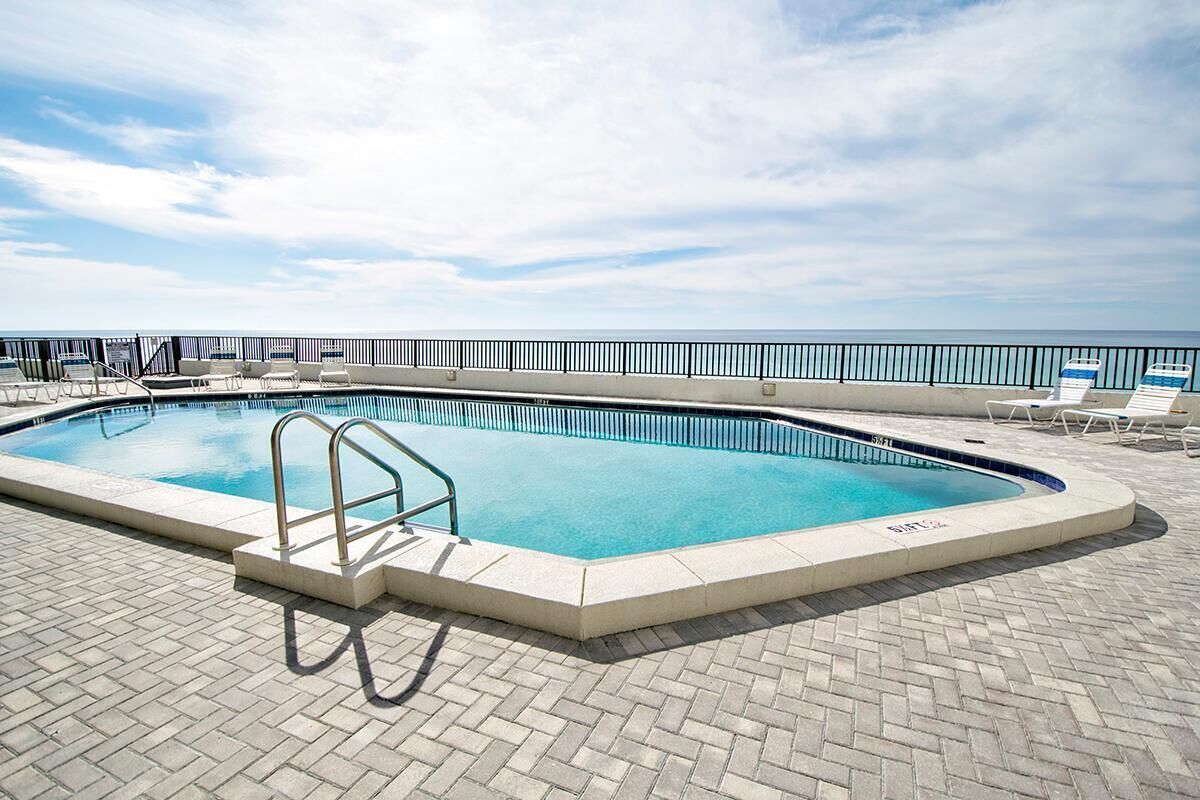 Una piscina rectangular con una escalera metálica, rodeada por un patio de ladrillo y una barandilla metálica.