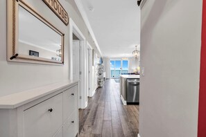 A hallway leading to a kitchen with a view of the outside. - Twin Palms 1802 (Panama City Beach)