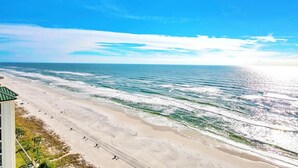 Une plage avec des vagues, un ciel dégagé et un bâtiment doté d’un toit végétalisé.