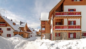 Un village enneigé, avec ses bâtiments traditionnels en bois, ses balcons et un ciel dégagé.