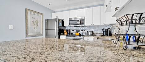 A modern kitchen with granite countertops, stainless steel appliances, and white cabinetry.