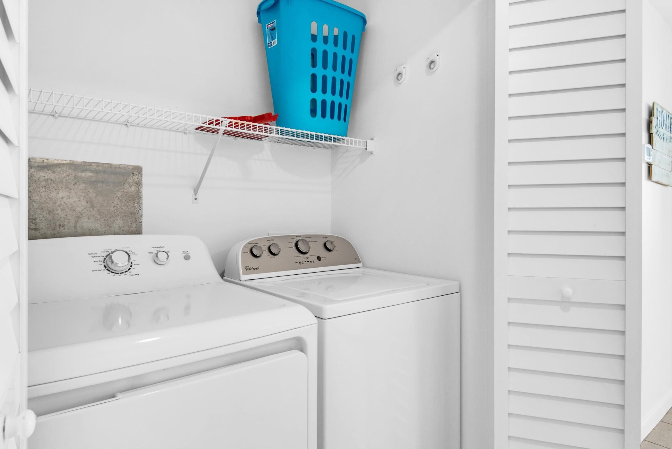 Une buanderie avec un lave-linge et un sèche-linge blancs, un panier à linge bleu et un étendoir métallique.
