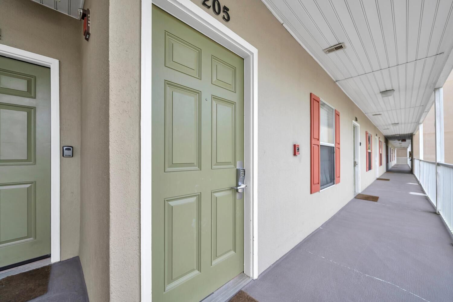 A corridor with green doors, numbered 205, and red-framed windows.