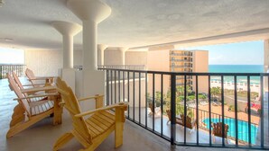 A balcony with wooden chairs, a pool, and a view of the beach and ocean.