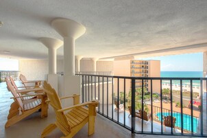 A balcony with wooden chairs, a pool, and a view of the beach and ocean.