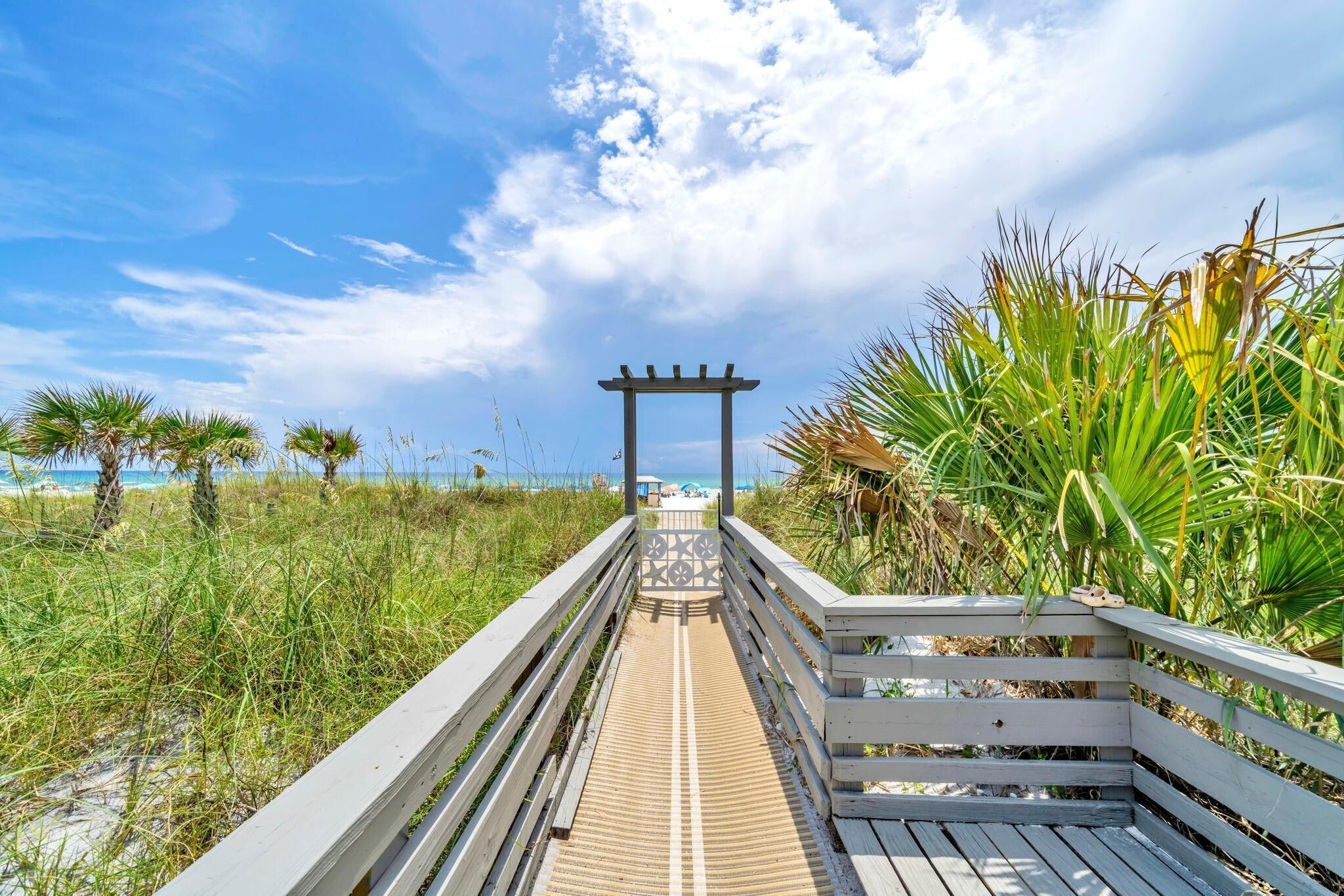 Een houten looppad dat naar een strand leidt, met een pergola.