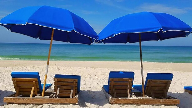 A beach with wooden lounge chairs and blue umbrellas.