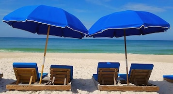 A beach with wooden lounge chairs and blue umbrellas.