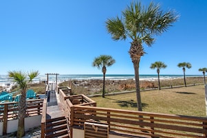 A wooden deck leading to beach chairs and a palm tree, overlooking the ocean.