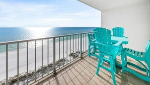 A balcony with turquoise chairs and a table overlooking a beach with a clear view of the ocean.