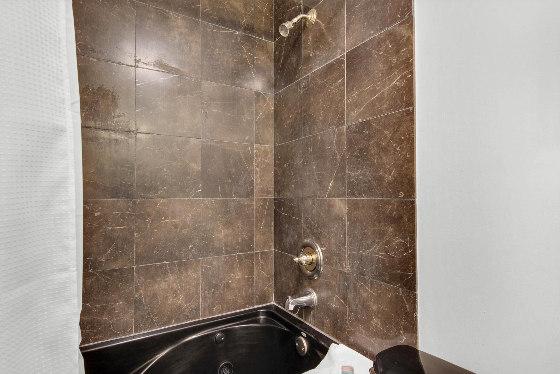 A bathroom with a black bathtub, a shower, and a wall-mounted faucet.