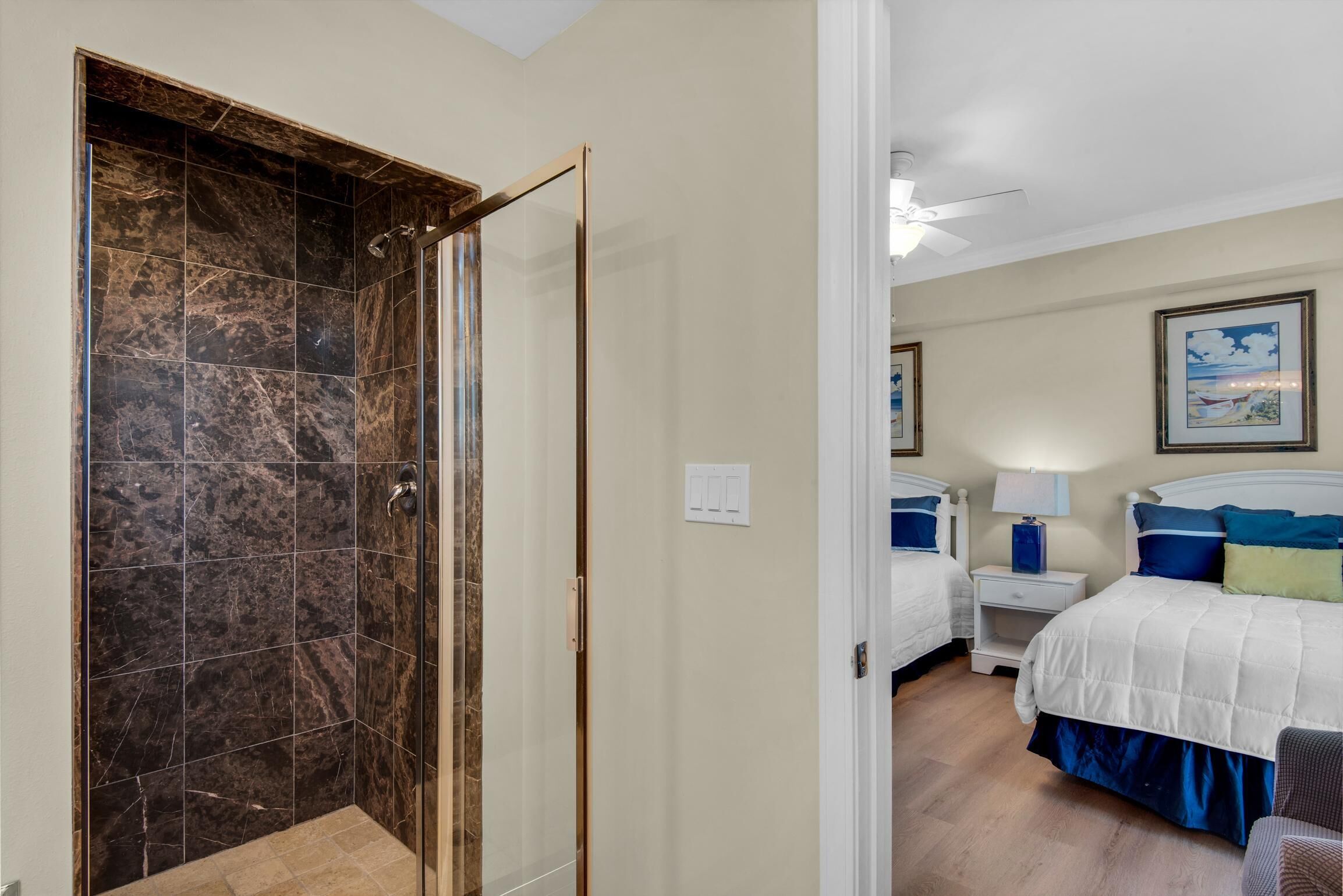 A hotel room with a shower, a bed with blue and white bedding, a nightstand with a lamp, and a framed picture on the wall.