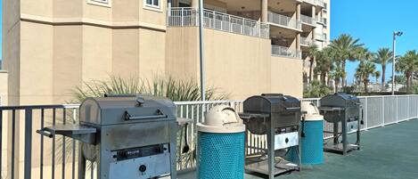 Outdoor barbecue grills and trash bins on a balcony with a building in the background.